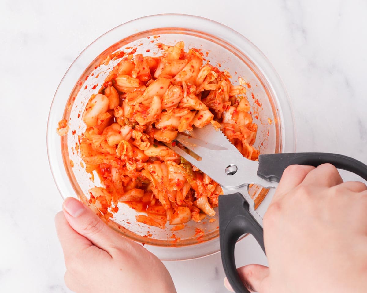 Cutting kimchi with scissors in bowl.