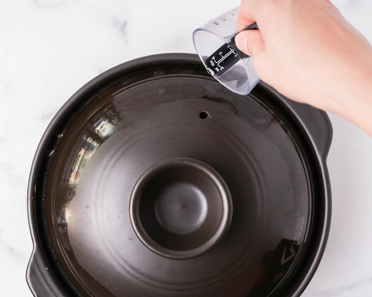 Pouring oil around clay pot lid.
