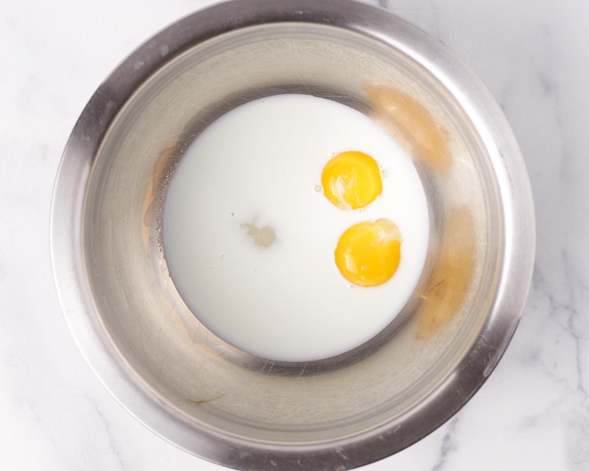 Adding milk, sugar, and egg yolks in bowl.