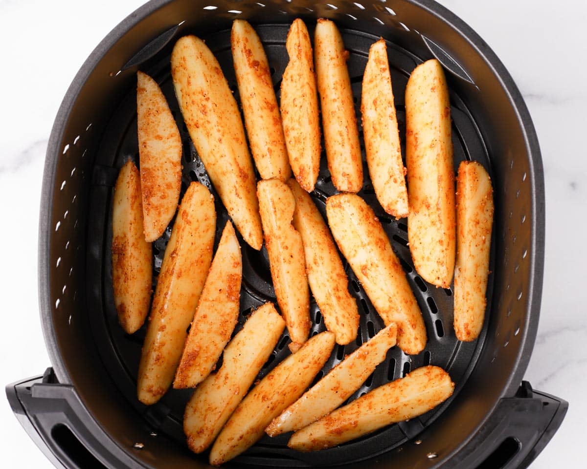 Placing potato wedges in air fryer basket.
