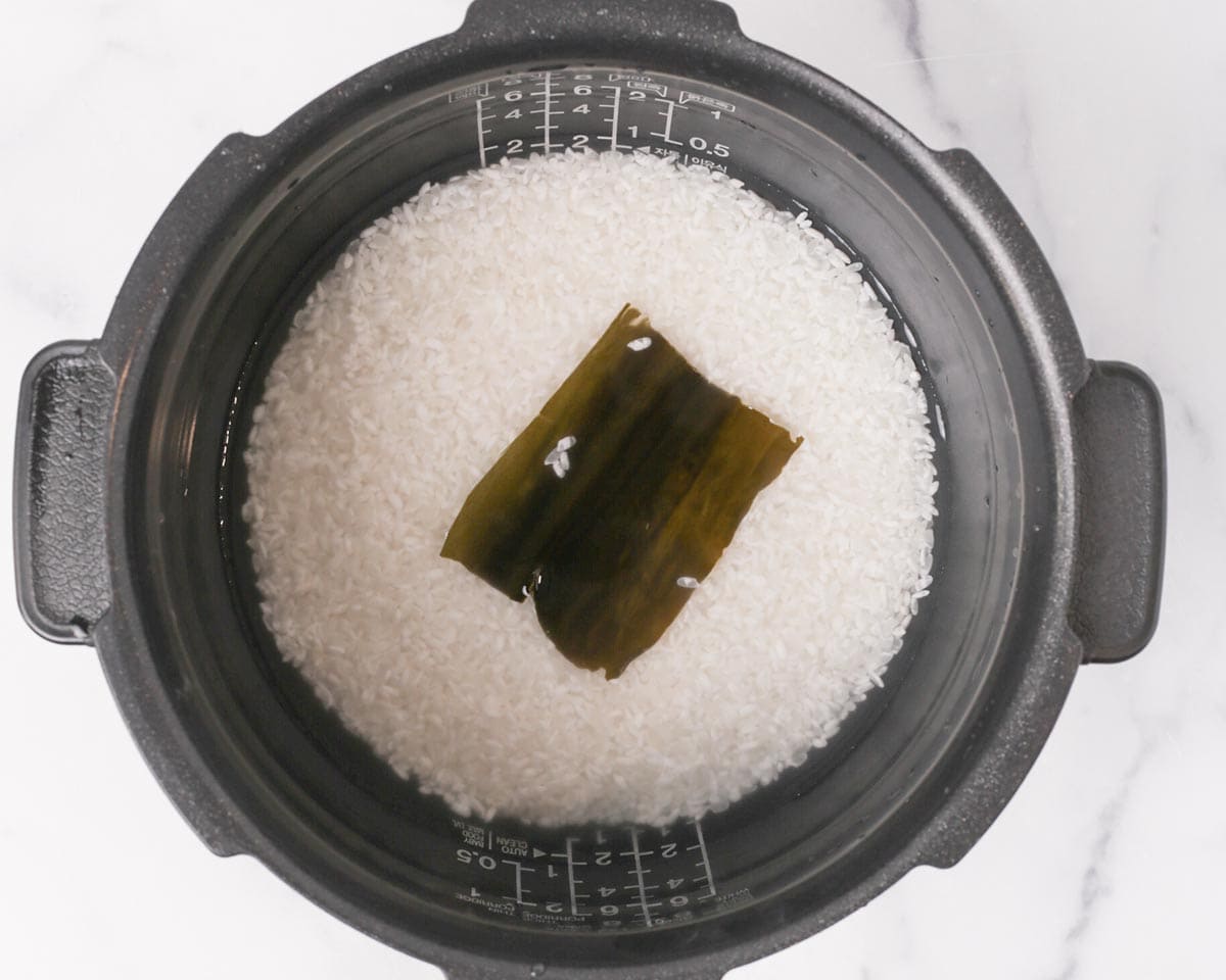 Raw rice and kombu in rice cooker pot.
