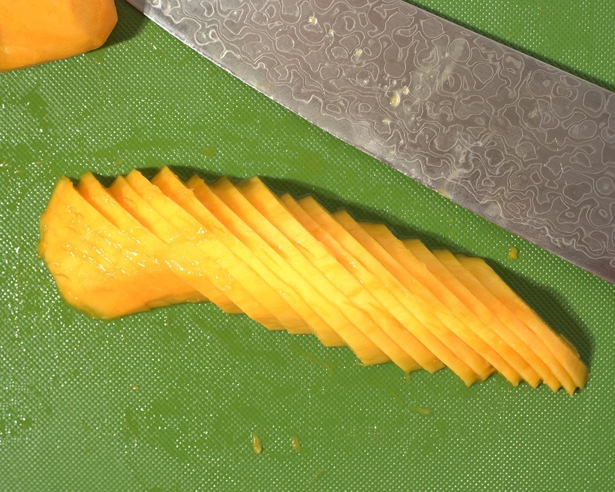 Cutting mango half into thin slices.