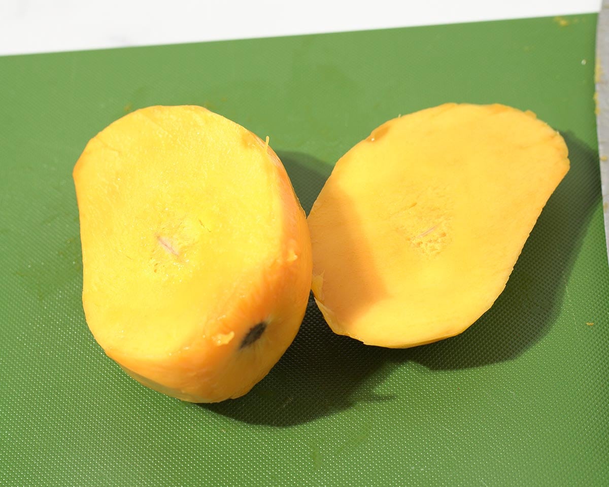 Cutting peeled mango in half.