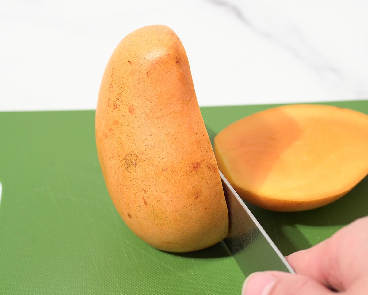 Cutting unpeeled mango in half.