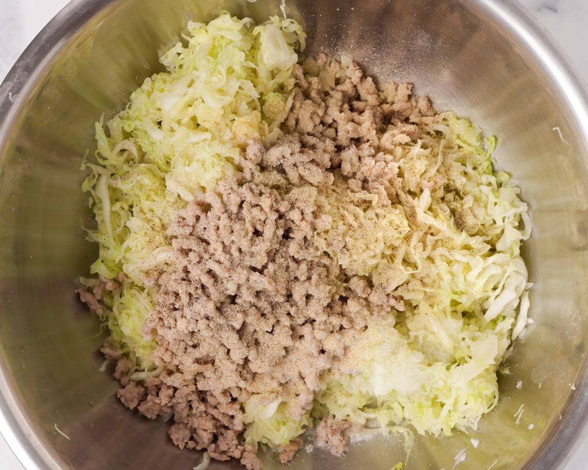 Adding cooked ground pork and seasonings to cabbage and celery.