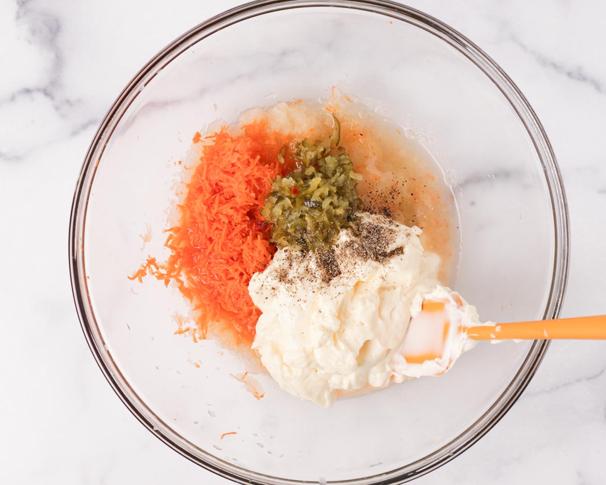 All the dressing ingredients in the bowl with grated carrots and onions.