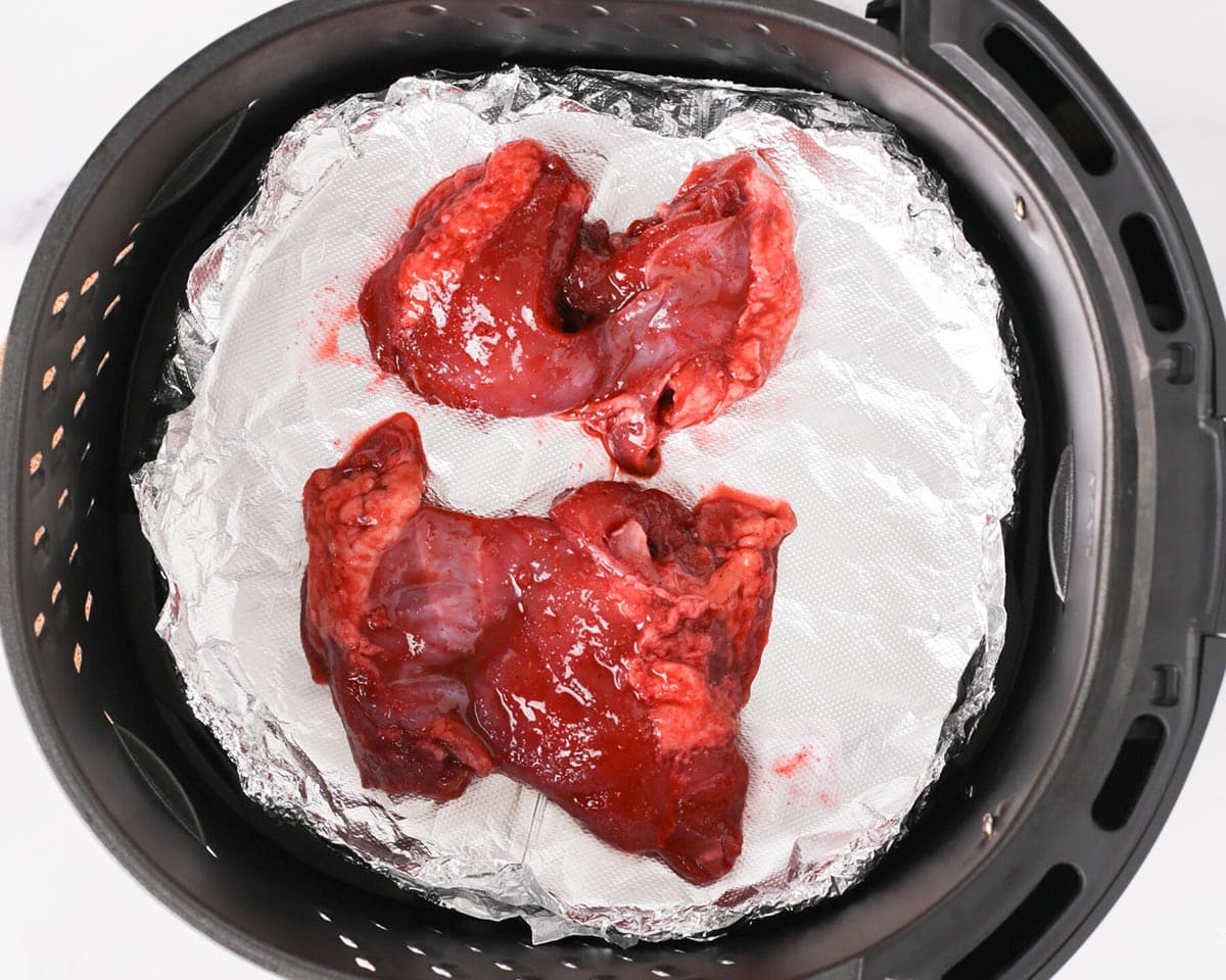 Placing the marinated chicken thighs in air fryer basket.