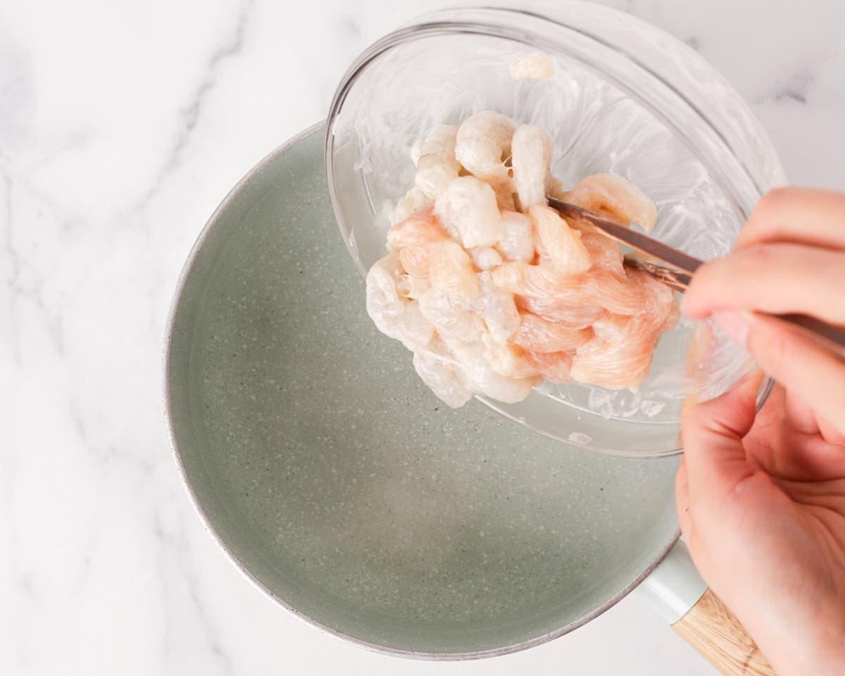 Adding marinated shrimps and chicken to a pot of hot water.