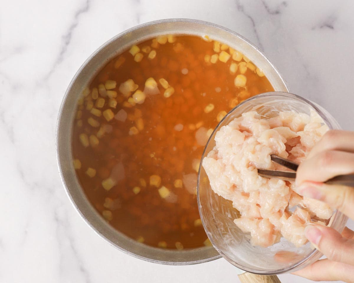 Adding seasoned diced chicken to the pot.