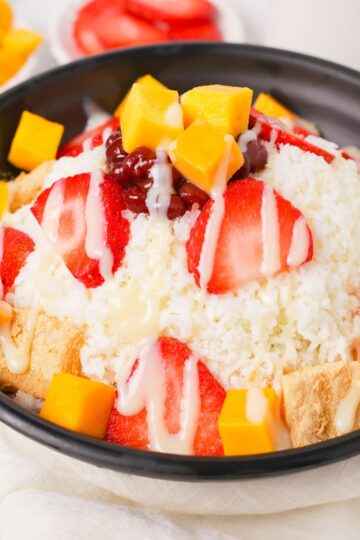 Bingsu in a bowl with different toppings and condensed milk.