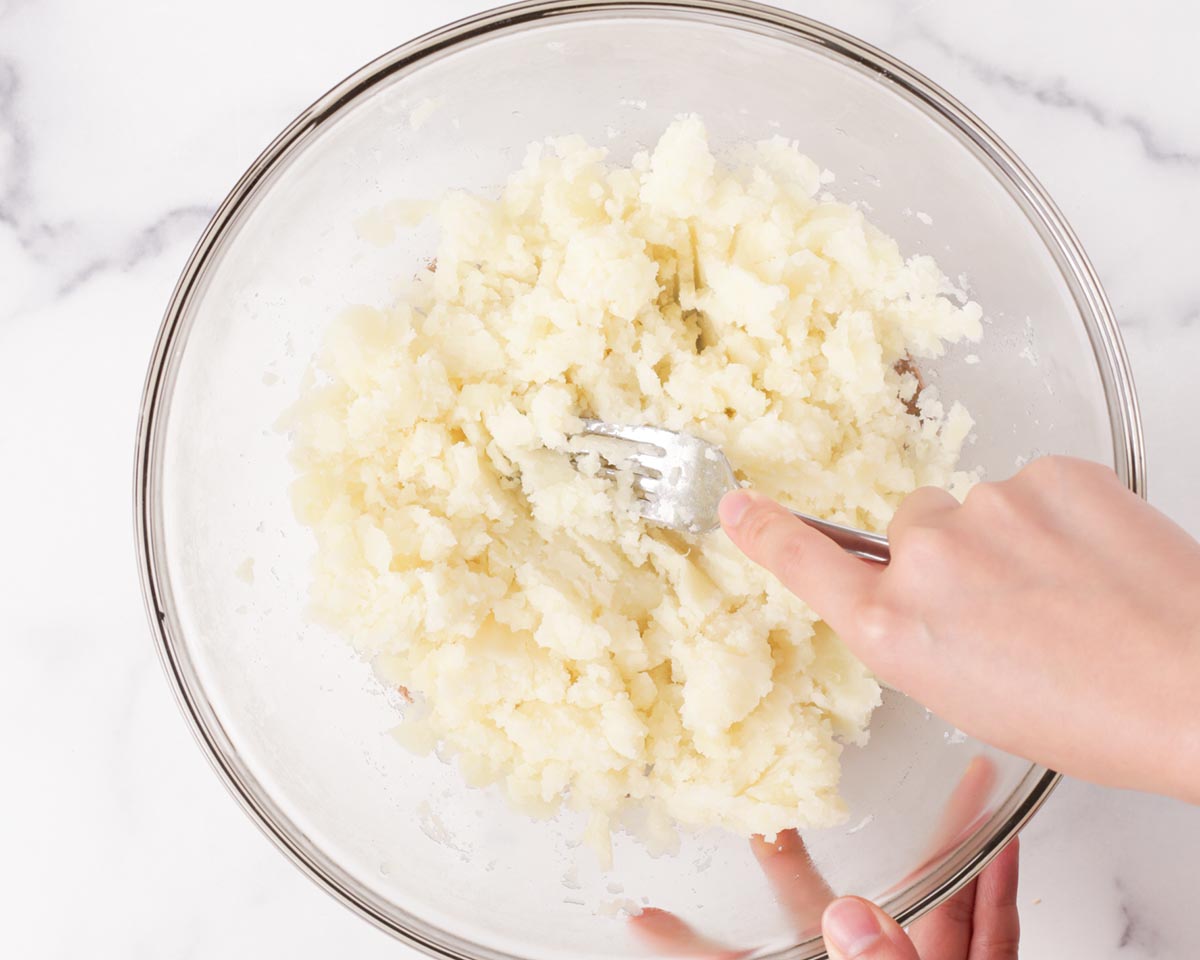 Mashing cooked potatoes with a fork.