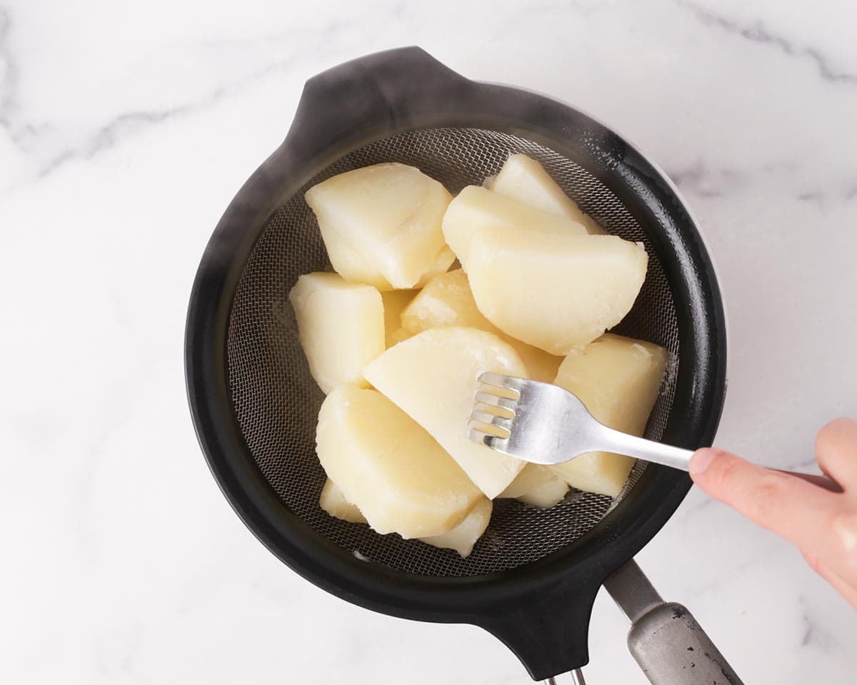 Stabbing the potato to show that it is fork-tender.