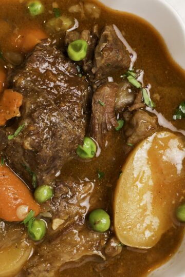 A bowl of beef stew with peas, carrots, and potatoes.