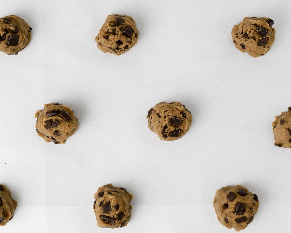 Balls of brown butter chocolate chip cookies arranged on a parchment lined sheet pan.