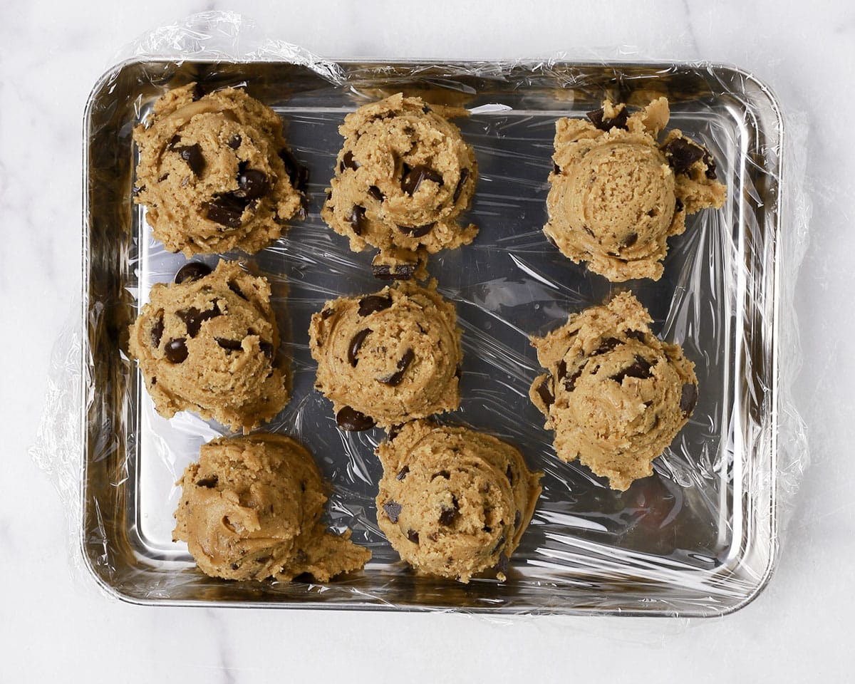 Brown butter chocolate chip cookies scooped and arranged on a plastic wrap lined sheet pan.